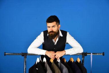 Tezgahtar ya da satıcı elbise askılarına yaslanır.