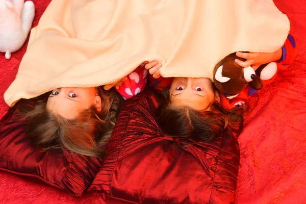 Παιδιά με μισοκρυμένες φάτσες ξαπλώνουν στο κρεβάτι, πάνω όψη. — Φωτογραφία Αρχείου