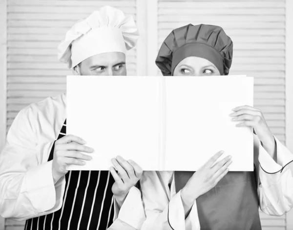 Erkek ve kadın şef açık kitabın arkasına yüzlerini gizlerler. Adam ve kız kitap tarifleri okudu. Mutfak konsepti. Aile tarifi öğrenir. Pişirme becerisini geliştirin. Kitap aile tarifleri. Pişirme kılavuzu. Tarife göre — Stok fotoğraf