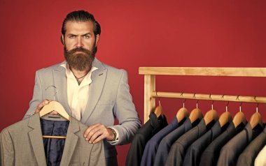 Vahşi sakallı erkek. Sakallı adam askıda ceketi seçiyor. Erkek giyimi konsepti. Adam giyim mağazasına alışverişe gider. Stüdyo atölyemiz herhangi bir moda tarzını sunar. Geniş erkek giysisi seçimi