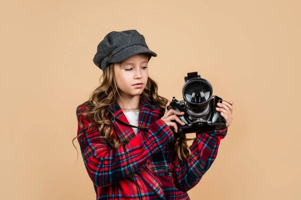 Happy kid in cap met stijlvolle kapsel dragen geruite jas gebruik vintage fotocamera voor het fotograferen, fotografie — Stockfoto