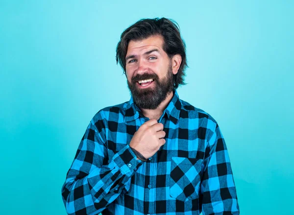 Um hipster barbudo brutal. Um tipo maduro com bigode na cara. expressar emoções humanas. homem feliz em camisa quadriculada. homem emocional no fundo azul — Fotografia de Stock