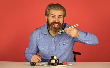 Evde akşam yemeği. hipster yemek çubuklarıyla suşi yer. Lezzetli suşi rulosu. Japonya 'da geleneksel ve sağlıklı yiyecekler. Japon suşi yemeği. Geleneksel Japon yemeklerini çubuklarla yiyen adam.