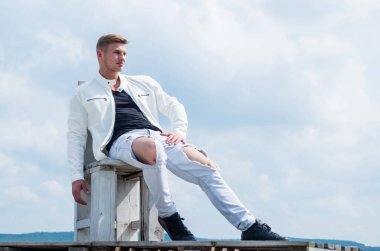 Rahatlamış seksi bakışlar. Seksi adam, bulutlu gökyüzüne otur. Yakışıklı adam açık havada rahat giyiniyor. Moda dolabı. Tatil zamanı. Eğlence etkinliği. Dolaşmak ve seyahat etmek. Bakım özgürlüğü