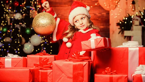 Criança menina feliz animado encontrar presentes perto da árvore de Natal. Feliz Natal! Feliz Natal! O miúdo usa chapéu de Pai Natal embrulhado na caixa de presente. O Pai Natal trouxe-me presentes. Felicidade e alegria. Conceito de infância feliz — Fotografia de Stock