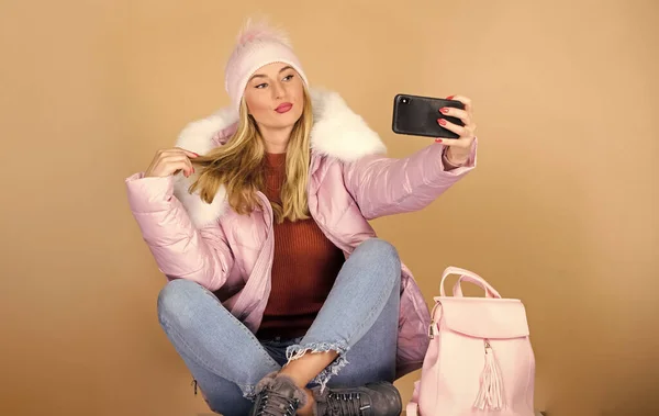 faux fur fashion. warm winter clothing. phone selfie. flu and cold season. Leather bag fashion. woman in beanie hat with backpack. happy winter holidays. web blogger. girl in puffed coat make selfie