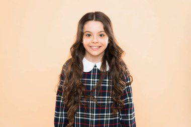 Mutlu gülümseyen çocuk portresi. Duygusal ifadeler. Sadece mutluyum. Küçük kız zarif damalı elbise. Çocuk uzun kıvırcık saçlı. Mutlu liseli kız üniforması. Çocukluk konsepti. Çocuk psikolojisi