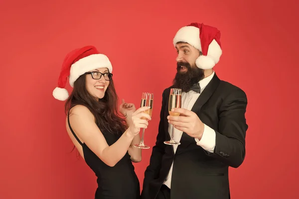 Szórakozzunk egy kicsit. Irodai buli. Téli parti. Boldog karácsonyt! Egy pár a céges bulin. Boldog új évet! Szakállas üzletember szmokingban és lány elegáns ruha ivás pezsgő piros háttér — Stock Fotó
