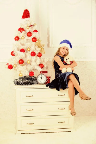 Best gift ever. Excitement replaced with strong feeling satisfaction. Happy new year concept. Kid sit near christmas tree hold teddy bear gift. Little girl santa hat satisfied christmas gift — Stock Photo, Image