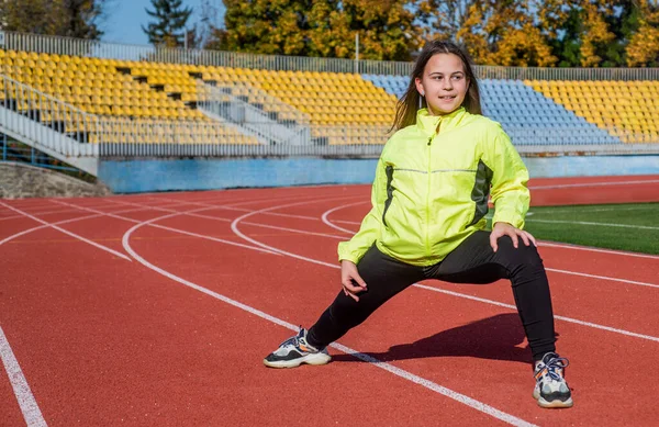 Criança fazer exercício em pista de corrida. infância saudável. treino ao ar livre ao ar livre. Corredor confiante. corpo flexível. menina adolescente aquecendo no estádio. miúdo de fato desportivo a esticar-se. Determinado a ganhar — Fotografia de Stock