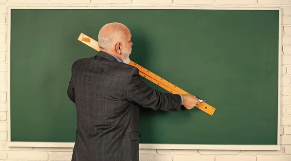 先輩先生は絵を描きながら定規を使います。ひげを生やした家庭教師の男が黒板に定規で描く。学校に戻って。学校の規律。教育と知識。高校時代の幾何学的形状 — ストック写真