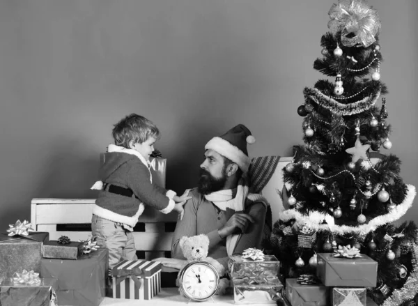 Kerstman en kleine assistent onder geschenkdozen in de buurt van kerstboom. — Stockfoto