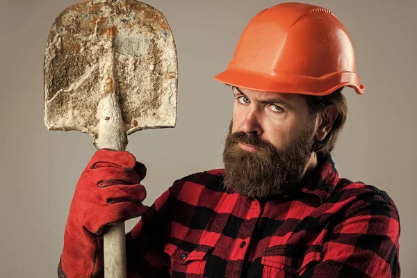 髭を生やした修理工。建設技術者だ。プロの建築家は手袋にシャベルを持ってる。修理と建物。真剣な男労働者は堅い帽子をかぶる。ヘルメットの残酷な建築家 — ストック写真