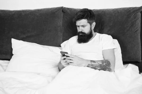 First of all. Bearded man texting sms in bed. Hipster send message using smartphone. Mobile message. Short message service. Mobile lifestyle. Social networks. Download application. Check email