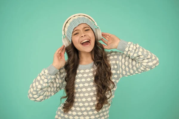 Muntre små barn strikket genser og øretelefoner. syngende unge med turkis bakgrunn. favorittsangene hennes. Glad jente liker vinterleker. Musikkstemning. sang for å motivere deg i kaldt vær – stockfoto