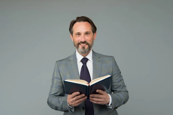 Profesor de școală fericit în costum formal ține lecție de predare carte deschisă fundal gri, literatură — Fotografie, imagine de stoc