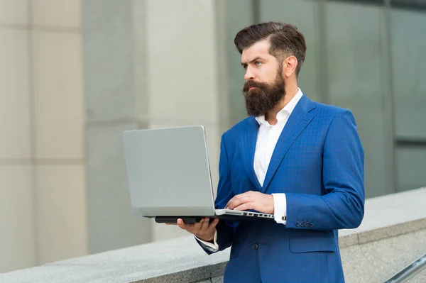 Brutalny biznesmen w formalnym garniturze służbowym używa laptopa do pracy online na świeżym powietrzu, e-biznes — Zdjęcie stockowe