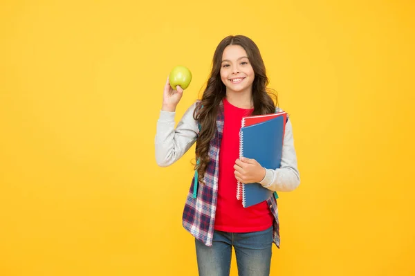 Μικρό παιδί κατέχει σχολικά βιβλία και φυσικό μήλο φρούτα κίτρινο φόντο, υγιεινή διατροφή — Φωτογραφία Αρχείου