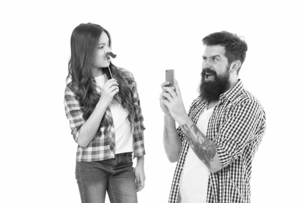 Tira uma foto. Equipa criativa. Homem barbudo tirar foto de criança pequena. Menina posando com adereços de bigode. Hipster usar câmera móvel smartphone. Celebração familiar. Sessão de fotos de família. Objectivos familiares — Fotografia de Stock