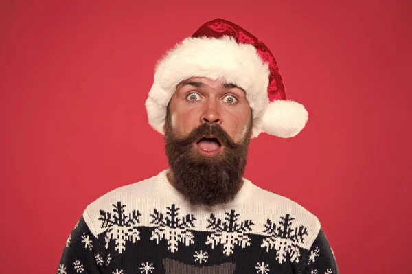 Novoroční párty. Neočekávané překvapení. překvapený vousatý muž Santa klobouk. brutální hipster oblíbený svetr červené pozadí. zimní prázdniny. překvapený knírek. portrét Santy s vousy — Stock fotografie