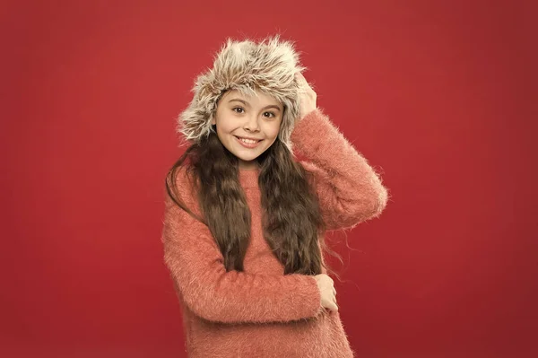 Feeling so cozy. Child long hair soft hat. Winter fashion concept. Warm hat for cold winter weather. Kid girl smile red background. Soft furry accessory. Winter season. Small fashionista concept