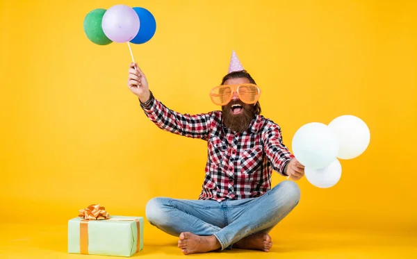 Homem barbudo brutal engraçado usar camisa quadriculada com barba exuberante e bigode segurar balões de festa e caixa de presente, férias — Fotografia de Stock