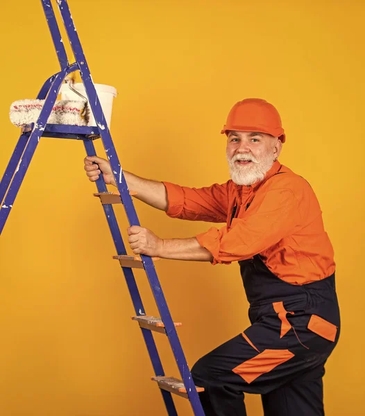 Boyacı merdiveni. Onarım yapmak için. İş elbiseli bir adam boş odaya duvar boyuyor. Boyalı kovayla şapkalı bir ressam. İnşaat işçisi boyama cephesi. termal yalıtım işe yarıyor