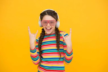 Havalı ve havalı. Sarı arka planda gülümseyen bir çocuk. hipster parti tarzı. Mutlu genç kız modern kulaklık takıyor. Komik çocuk müzik dinler. Göz kamaştırıcı gözlüklerdeki güzellik. çocukluk mutluluğu