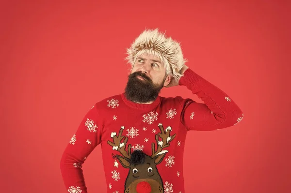 Need prepare for holidays. thinking hipster in earflap hat. winter holiday activity. warm clothes in cold weather. happy new year. bearded man on red background. funny man beard in knitted sweater — Stock Photo, Image