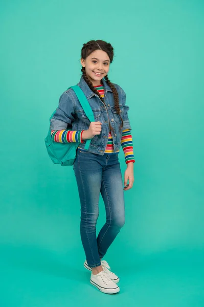 Szczęśliwe dziecko z długimi warkoczami nosić torbę podróżną noszenie casual streetwear niebieskie tło, moda — Zdjęcie stockowe