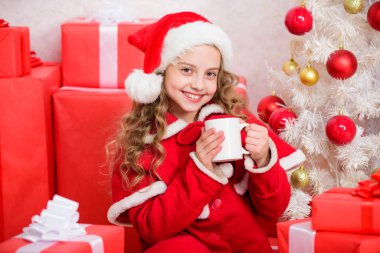 Çocuk Noel Baba şapkası kakao içeceğinin tadını çıkarıyor. Tatil sezonunu ısıtmak için mükemmel bir yol. Küçük tatlı kız Noel 'i kutlarken sıcak içecekle bardağı tutuyor. Noel arifesinde sıcak kakao. Kakao en sevdiği içecek.