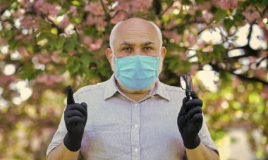 Kurallara uy. Tıbbi maske ve eldiven giymiş kıdemli bir adam. Parktaki sakura ağacı. Coronavirus kapanışı sırasında hayat. Hastalık korkusu. Virüsle savaşma stratejisi. Halka açık yerlerde ziyaret yasağı
