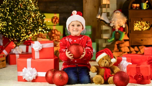 Glückliches Kind Weihnachtsmann Hut. Sohn bereit, Winterurlaub zu feiern. kleiner Junge begeistert mit Geschenk. Kinder halten dekorativen Ball. Bärenspielzeug für Weihnachten. Frohe Weihnachten. frohes neues Jahr — Stockfoto