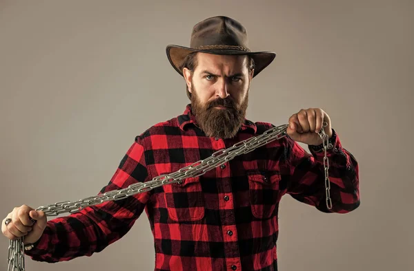 Brutal man in cowboy hat with chain. chained up in chains. bearded man has aggressive look. express his strength. male power and masculinity. mature hipster break chain. fetter — Stock Photo, Image