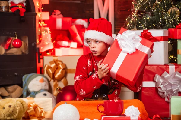 Niño pequeño niño feliz encontrar regalos cerca del árbol de Navidad. Tienda de regalos. Kid santa hat cajas de regalo de Navidad. Feliz navidad. La belleza del invierno. Ocio y actividad. Día de boxeo. Intrigado lindo santa — Foto de Stock