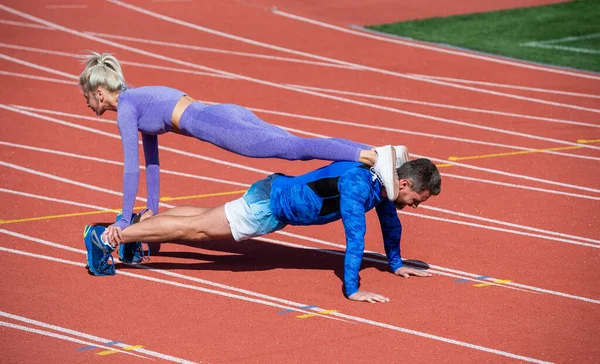 Spor salonundaki erkek ve kadın sporcu birlikte antrenman yapıyor. Tahtada duruyorlar ve spor kıyafetleri giymiş, sağlıklı bir yaşam tarzı olan stadyum yarış pistinde şınav çekiyorlar. — Stok fotoğraf