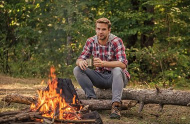 Adam parkta dinleniyor. Yürüyüş macerası. Turizm kampında piknik. Piknik ateşinde kahve içmek. Ateşin yanında ısının. Açık hava aktivitelerinde korucu. Yürüyüş ve kamp. Piknik haftasonunu doğada geçirmek