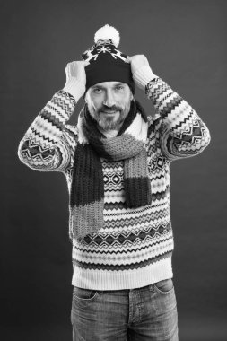 Örgü aksesuarlar. Olgun erkek kırmızı arka plan. Soğuk hava konsepti. Kışın sakallı adam. Beyaz adam kalın kıyafetler giyer. Kış trendleri. Şapka atkısı ve kazak. Kış örgüsü.