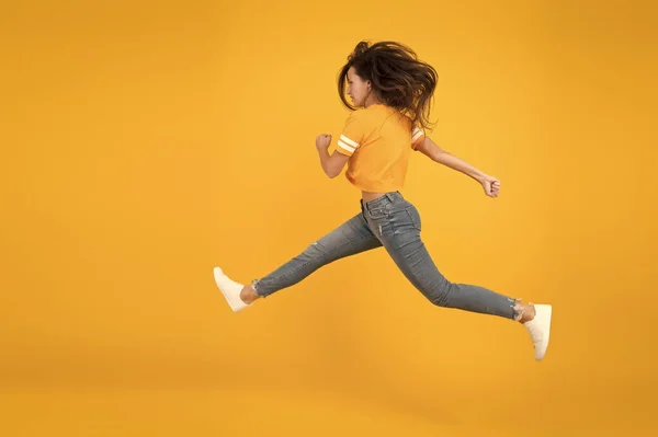 Uma mulher energética a correr ou a saltar. Calça jeans Skinny combina com ela. Menina sexy fundo amarelo. Menina sensual em estilo casual. Sinta a energia interior. Menina bonita com cabelo comprido. Estilo de moda. Beleza e maquiagem — Fotografia de Stock