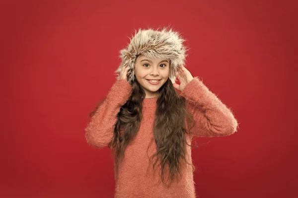 Κράτα το κεφάλι σου ζεστό. Ζεσταίνομαι. Παιδικό μακρυμάνικο καπέλο. Χειμερινή μόδα. Ζεστό καπέλο για κρύο χειμώνα. Μικρό κορίτσι κόκκινο φόντο. Μαλακό γούνινο αξεσουάρ. Χειμερινή περίοδος. Έννοια αγορών — Φωτογραφία Αρχείου