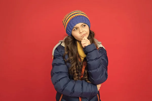 Vinterdrömmar. omtänksamt barn i varma vinterkläder. säsongsbetonat mode för barn. liten skönhet röd bakgrund. liten flicka puffer jacka och stickad hatt. bry dig om dig själv i kallt väder — Stockfoto