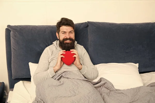 Dulce corazón. sorpresa de la mañana de su San Valentín. Feliz día de San Valentín. barbudo hombre celebrar decoración corazón en la cama. corazón lleno de amor. empezar el día con romántico. hipster con presente —  Fotos de Stock