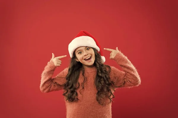Entzückende Mädchen mit langen lockigen Haaren tragen Weihnachtsmann Hut roten Hintergrund. Tage zählen bis Weihnachten. Weihnachtsfeier. Weihnachtseinladung. Positivitätskonzept. Gute Laune. Winterliche Traditionen — Stockfoto