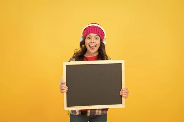 Estudante ouvir música em fones de ouvido. O miúdo adolescente segura no quadro negro. de volta à escola. anúncio e promoção. auto-educação. menina feliz fundo amarelo, espaço cópia. informando sobre vendas — Fotografia de Stock