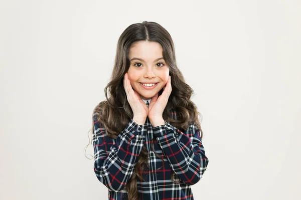 Cuidados faciais. Cuida do cabelo dela. criança tem cabelo encaracolado longo. depois da visita ao cabeleireiro. estudante feliz em uniforme elegante. de volta à escola. menina pequena vestido xadrez. conceito de moda infantil — Fotografia de Stock