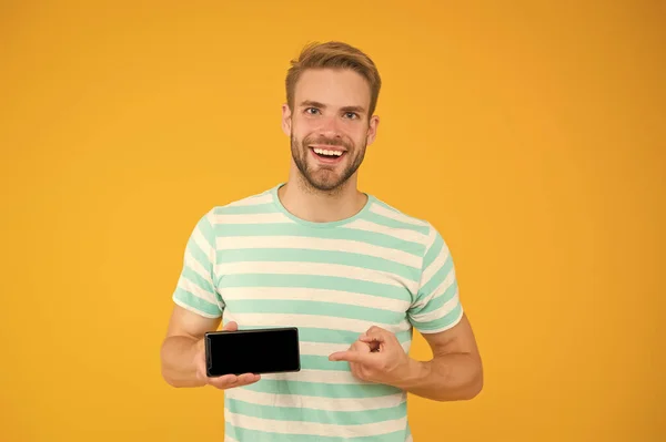 Das beste Telefon für Sie. Glücklicher Kerl, der auf den gelben Hintergrund des Smartphones zeigt. Hinweis auf Werbung. Zeigefinger. Zeigende Geste. Top-Wahl. Es wird Ihnen das Leben tatsächlich erleichtern — Stockfoto