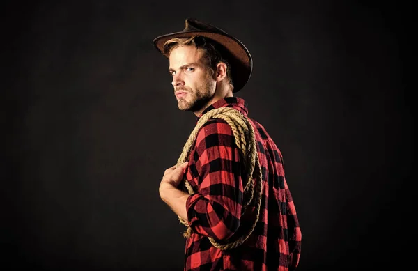 A vida ocidental. Homem de chapéu segura corda. Ferramenta de laço de cowboy americano. Lasso é usado em rodeios como parte de eventos competitivos. Homem unshaven cowboy fundo preto. Lasso pode ser amarrado ou embrulhado — Fotografia de Stock