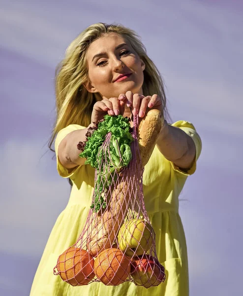 Reusable eco bag for shopping. Woman holding string shopping bag with fruits and bread on sky background. Zero waste concept. girl in dress with string bag shopper. bag with groceries. Raw food diet