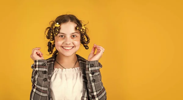 Kind macht Frisur. kleines glückliches Mädchen mit Lockenwicklern im Haar. Stoffmaske unter den Augen für Schönheit. niedliches Kind, das mit Flecken unter den Augen steht. Modell für Kindermode. Kopierraum — Stockfoto