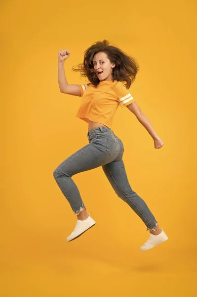 Voel innerlijke energie. Een energieke vrouw die rent of springt. Skinny jeans staat haar goed. Sexy meisje gele achtergrond. Sensueel meisje in casual stijl. Mooi meisje met lang haar. Modestijl. Schoonheid en make-up — Stockfoto